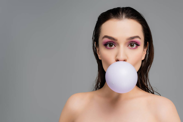 brunette woman with bare shoulders blowing bubblegum isolated on grey - Photo, Image