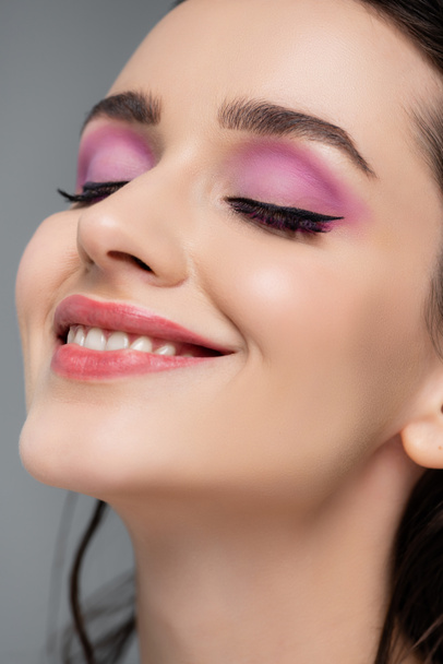 close up of brunette woman with pink eye shadows smiling isolated on grey - Fotoğraf, Görsel