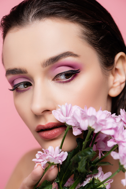 primer plano de la joven sensual mujer mirando hacia otro lado cerca de flores aisladas en rosa - Foto, Imagen