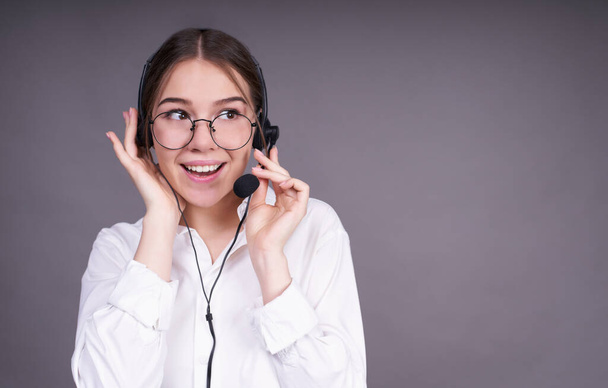 Attractive smiling young Caucasian girl in round glasses works in the contact center, support, wears a phone headset, smiles and helps the client. Copy space. - Photo, image
