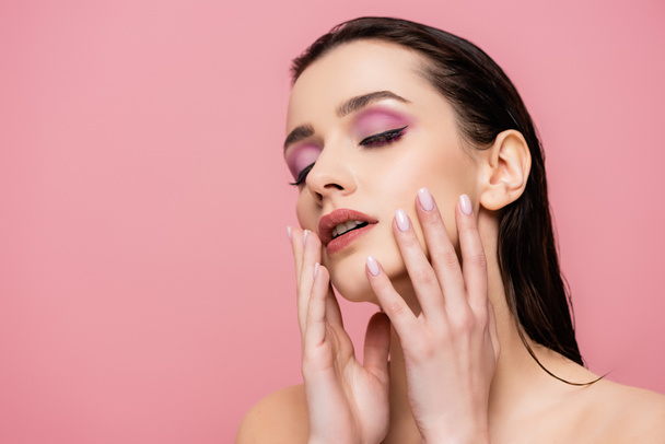 young woman with bare shoulders and makeup touching face isolated on pink  - Photo, Image