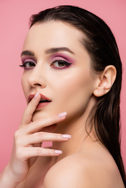 sensuele vrouw met blote schouders en make-up aanraken lippen geïsoleerd op roze  - Foto, afbeelding