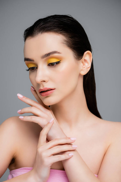 mladá brunetka žena se žlutým make-up pohledu pryč izolované na šedé - Fotografie, Obrázek