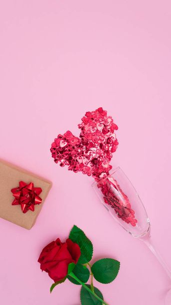 Красные сердца вытекают из бокала шампанского, розы и подарка. Розовый фон, вид сверху. Концепция Дня Святого Валентина. - Фото, изображение