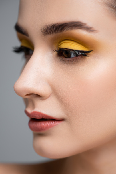 close up of young woman with yellow eyeshadow looking away isolated on grey - Photo, Image