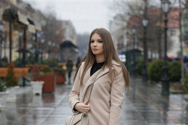Outdoor portret van jonge stijlvolle vrouw in kameel jas in de stad op een regenachtige dag - Foto, afbeelding