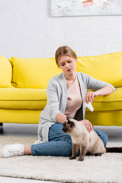 Woman with allergy holding napkin and petting siamese cat at home  - Photo, Image
