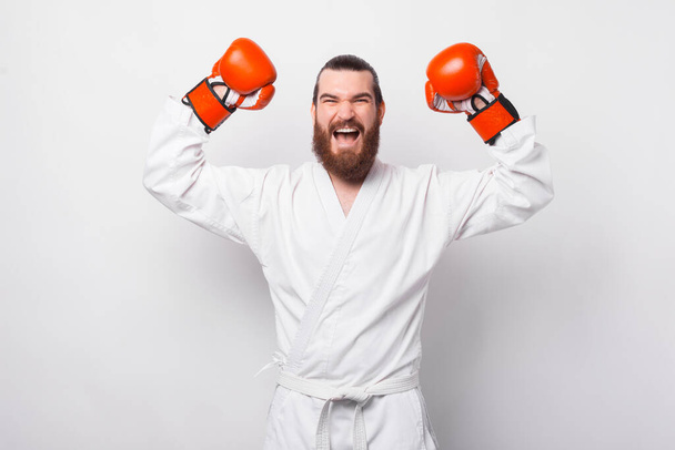Amazed excited bearded man in taekwondo dobok celebrating over white background - Photo, Image