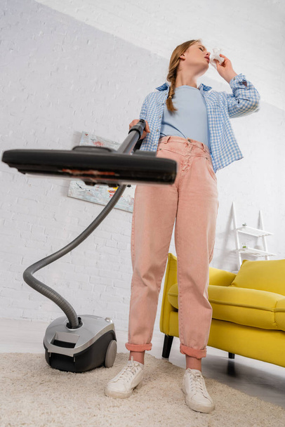 Low angle view of woman with allergy holding napkin and vacuum cleaner on blurred foreground  - Photo, Image