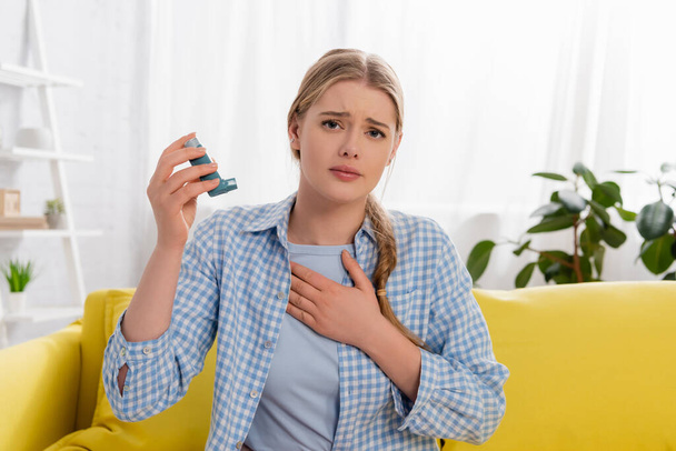 Unzufriedene Frau mit Allergiereaktion hält Inhalator auf Couch  - Foto, Bild