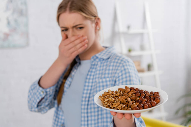 Plaat met noten in de hand van een vrouw met allergie op wazige achtergrond  - Foto, afbeelding