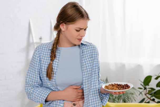 Αναστατωμένη γυναίκα με αλλεργία κοιτάζοντας πιάτο με ξηρούς καρπούς - Φωτογραφία, εικόνα