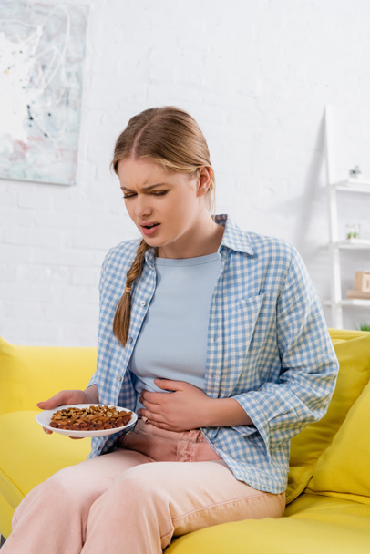 Хвора жінка з алергією тримає тарілку з горіхами на дивані
  - Фото, зображення