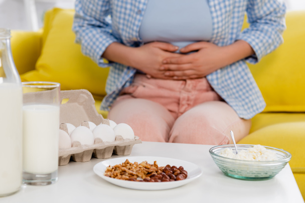 Cropped view of milk, eggs, cottage cheese and nuts near woman with allergy on blurred background  - Zdjęcie, obraz