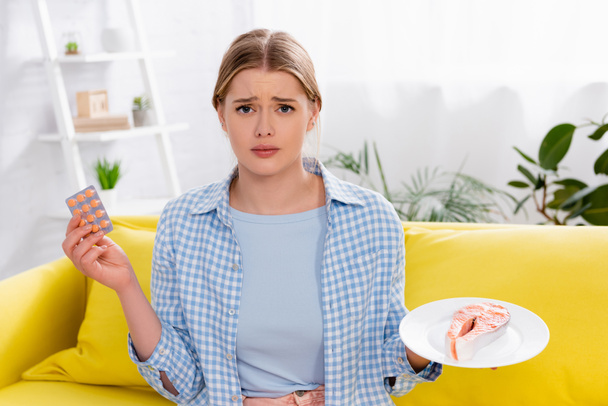Sad woman with allergy holding pills and salmon  - Photo, Image