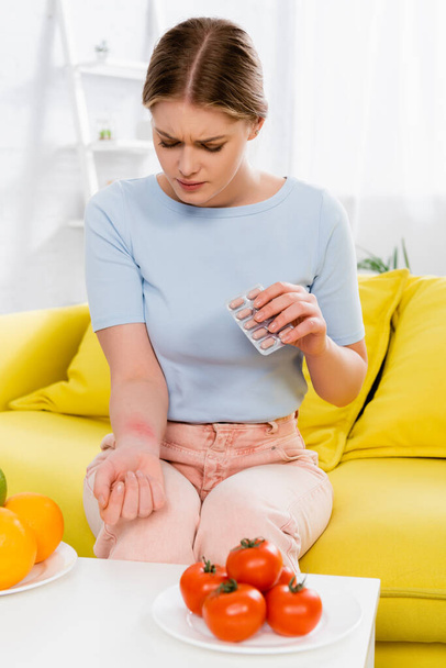 Femme allergique tenant des pilules près des tomates et des oranges au premier plan flou  - Photo, image
