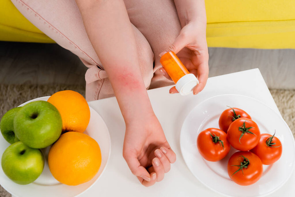 Vue recadrée de la femme allergique tenant des pilules près des fruits frais et des tomates  - Photo, image