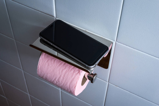 Mobiltelefon a WC-ben rózsaszín WC-papír ellen fehér csempe háttér .koncepció függőség telefon - Fotó, kép