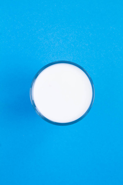 Vista superior do leite em um copo no centro do fundo azul. Localização vertical. - Foto, Imagem