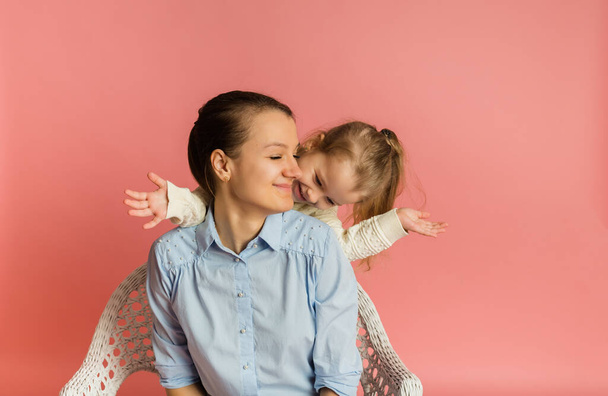 blonde daughter having fun with her mom on a pink background with a place for text - Фото, изображение