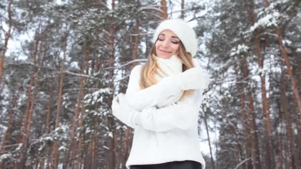 Красивая улыбающаяся девушка в зимнем лесу. Поза в белом свитере, шляпе и варежках - Кадры, видео