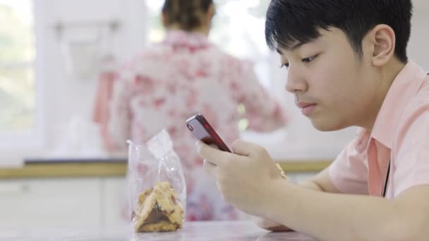 Asiático menino do ensino médio está jogando jogo online em seu telefone celular em casa. - Filmagem, Vídeo