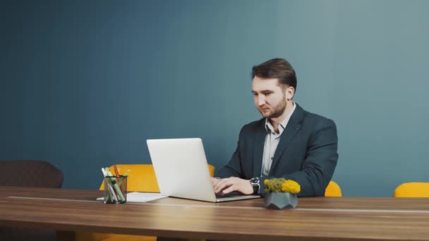 Jonge man met baard programmeur Kaukasisch uiterlijk, zittend en werkend op een laptop. Werk en communicatie op de computer op kantoor of thuis. Het concept van telewerken. - Video