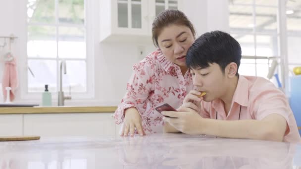 Ασιάτης μαθητής λυκείου με τη μητέρα του παίζουν online παιχνίδι στο κινητό του τηλέφωνο στο σπίτι. - Πλάνα, βίντεο