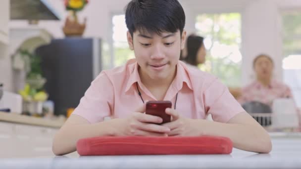 Ασιατικό γυμνάσιο αγόρι παίζει online παιχνίδι στο κινητό του τηλέφωνο στο σπίτι. - Πλάνα, βίντεο