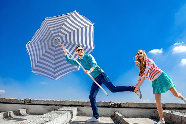 Funny and young couple have fun with beach umbrella on the roof  - Foto, Bild