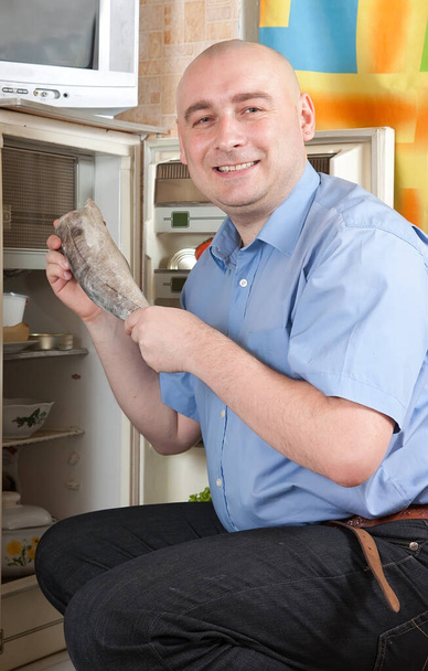 человек кладет сырую замороженную рыбу в холодильник дома - Фото, изображение