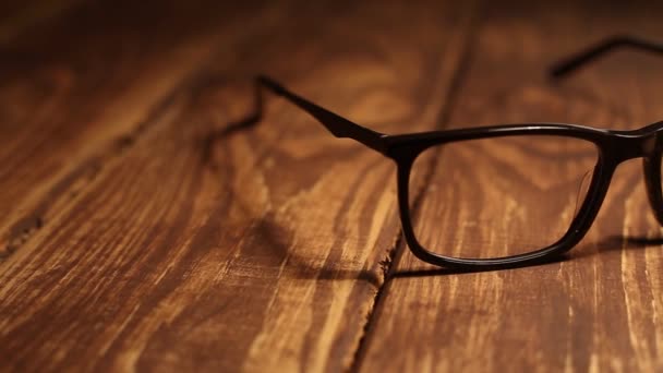 Las gafas para la vista yacen sobre una mesa de madera. La cámara panorámica horizontalmente - Metraje, vídeo