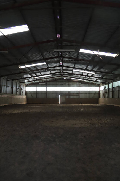 Foto de uma sala de equitação interior vazia para cavalos e cavaleiros. A escola de equitação é adequada para curativos e pular cavalos durante todo o dia - Foto, Imagem