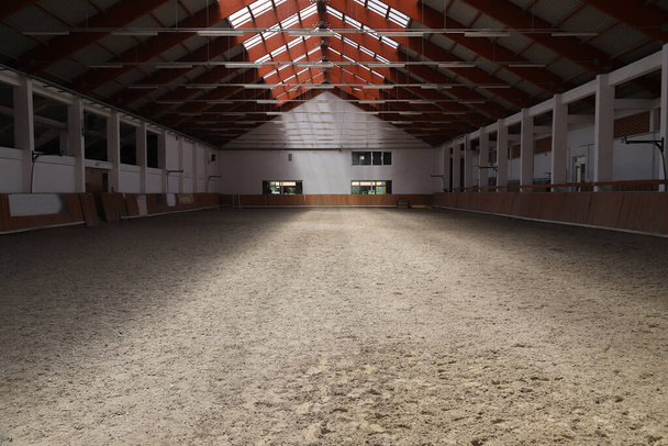 Photo of an empty indoor riding hall for horses and riders. The riding school is suitable for dressage and jumping horses all day - Photo, Image