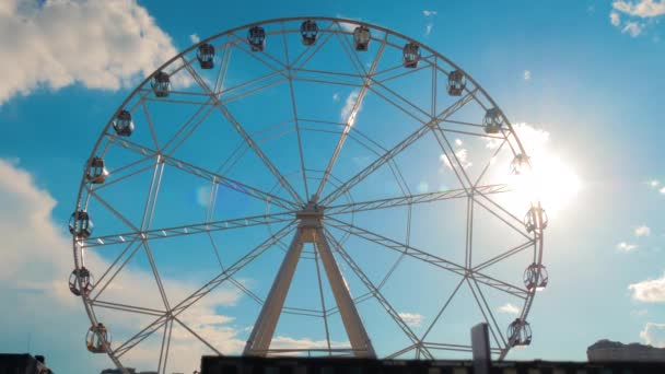 Силуэт колеса обозрения, вращающегося против голубого неба с облаками: вспышка линзы солнца - Кадры, видео