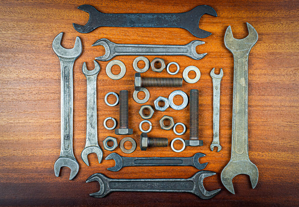 Різні старі ріжкові ключі, болти, горіхи та шайби в квадраті на фоні текстури коричневої деревини
 - Фото, зображення