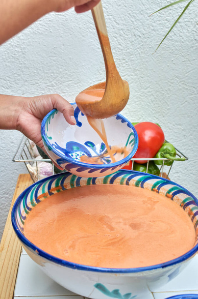 Gazpacho, andalusische und einige Zutaten zu seiner Zubereitung, wie Tomaten, Knoblauch und Zwiebeln, Gurken, auf einem weißen rustikalen Tisch, serviert in traditionellen andalusischen glasierten Keramiktellern - Foto, Bild