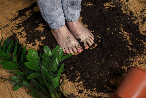 Barefoot child standing on the ground scattered from a flowerpot. High quality photo - Photo, Image