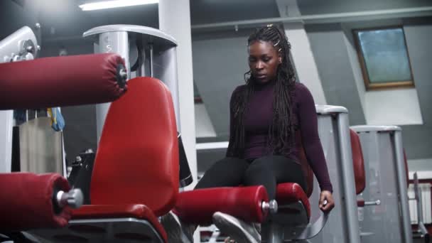 Een Afrikaans-Amerikaanse vrouw die traint in een sportschool met een fitnesstoestel en haar benen leegpompt. - Video