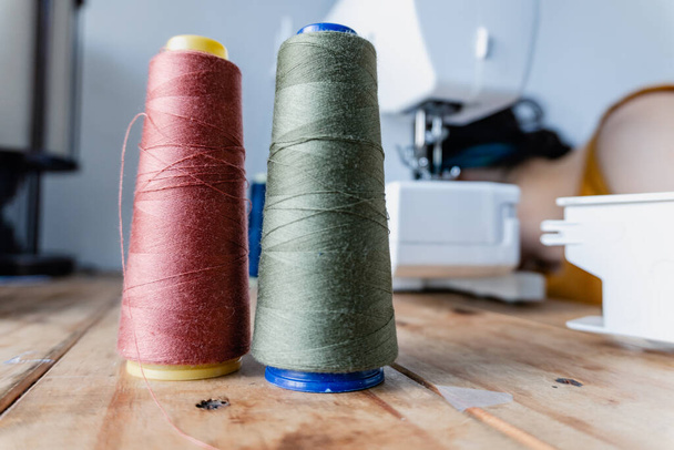 bobbins of cotton and polyester thread in green and Vinotint color with electronic sewing machine background. sewing from home by a woman. entrepreneurship. - Photo, Image