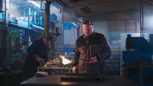 Handyman with autogenous welding troubles in his workshop while he's trying to solve over some small work problem with his equipment. His colleague can be noticed in the back working on his grinding task. - Footage, Video