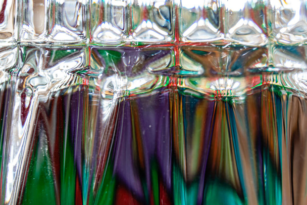 Παιδική χαρά του φωτός δει πολύ κοντά σε ένα ανεστραμμένο ποτήρι ουίσκι με ένα πολύχρωμο κηροπήγιο - Φωτογραφία, εικόνα
