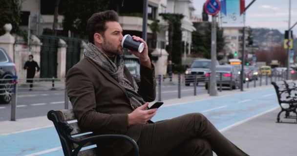 Man met behulp van smart phone.Businessman On Park Bench met koffie met behulp van mobiele telefoon - Video