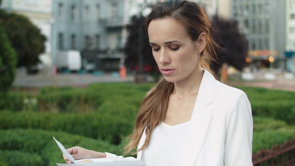 Портрет вдумчивой деловой женщины, ищущей данные в бумагах на открытом воздухе. - Фото, изображение