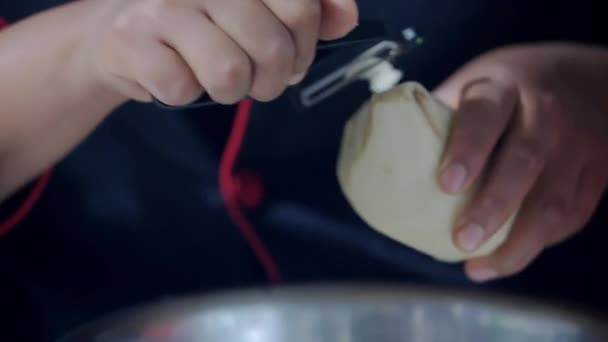 Τα χέρια του θηλυκού μάγειρα ξεφλουδίζει αργά μια πατάτα - Πλάνα, βίντεο