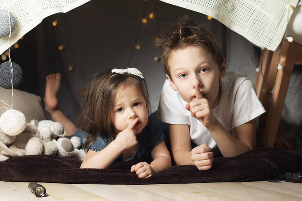 Geschwister liegen in Hütten aus Stühlen und Decken. Bruder und schwester zeigen stumm zeichen spielen zu hause - Foto, Bild