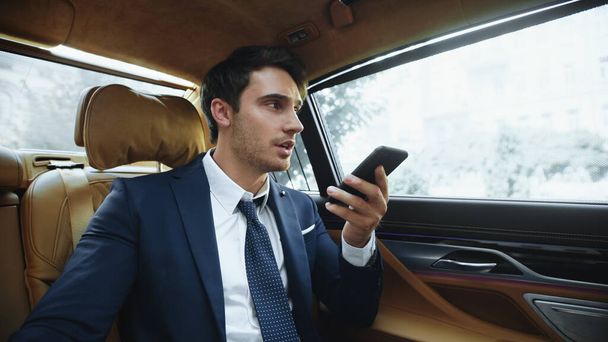 Focalizzato maschio professionale messaggio vocale di registrazione per smartphone in auto moderna. - Foto, immagini