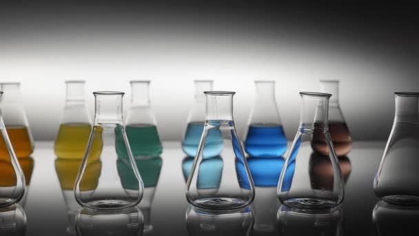 Frascos de laboratorio llenos de líquido de color vacío y mezclado que reflejan en la mesa. - Metraje, vídeo