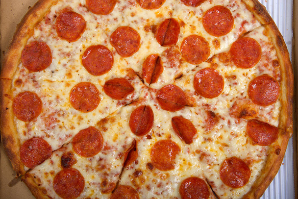 Top view lapos feküdt egy egész szeletelt pepperoni pizza a dobozban. - Fotó, kép