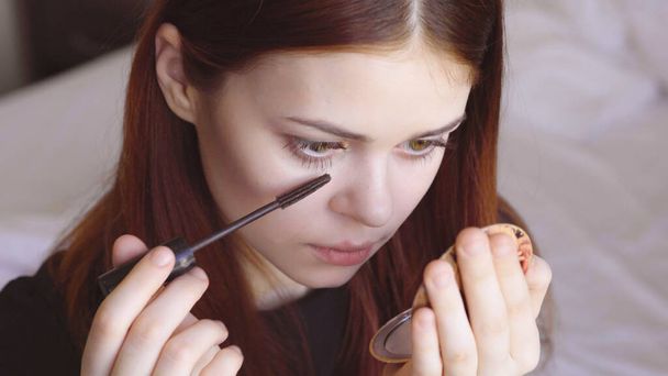Frau malt Wimpern mit Spiegel in der Hand zur Selbstpflege Weiblichkeit - Foto, Bild